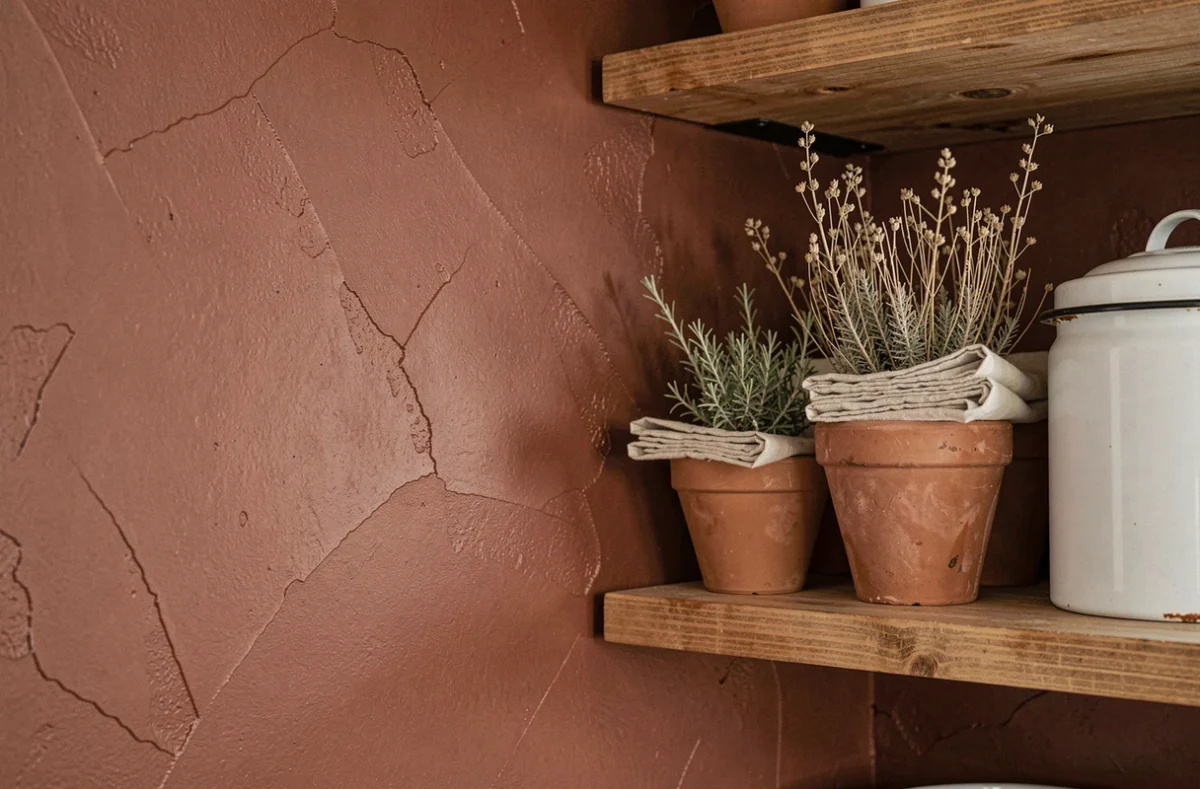 Détail de mur de cuisine peint en brun rouille avec étagères en bois et objets en terre cuite pour une ambiance chaleureuse