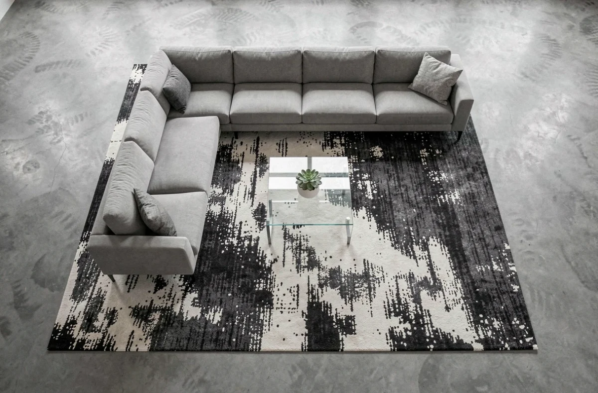 Vue aérienne d'un grand tapis abstrait sous un canapé d'angle dans un salon contemporain au sol en béton